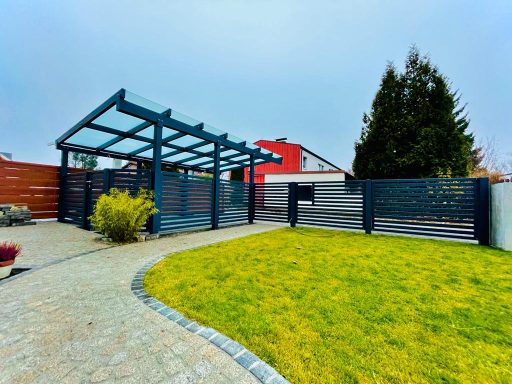 Eingezäunter Garten mit grünem Rasen, Steinweg und überdachtem Sitzbereich.